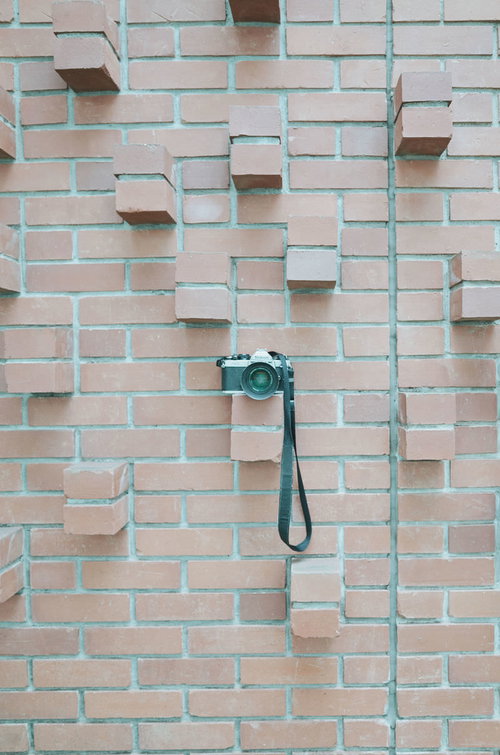 レンガ壁に飾られたクラシックカメラ、ストラップ付き