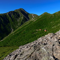 南アルプスの稜線に傾斜して立つ山小屋と赤石岳の写真