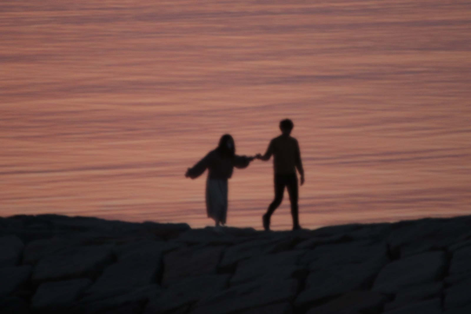 夕焼けの海岸で手を繋いで立つカップルのシルエット