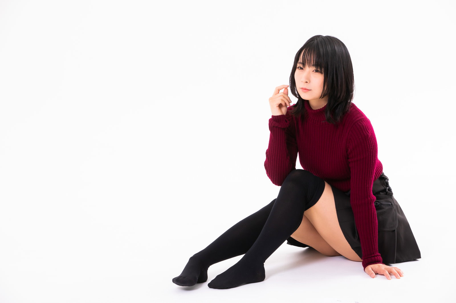 黒いハイソックスと黒いスカートの女性が地べたに腰を下ろしている［モデル：にゃるる］