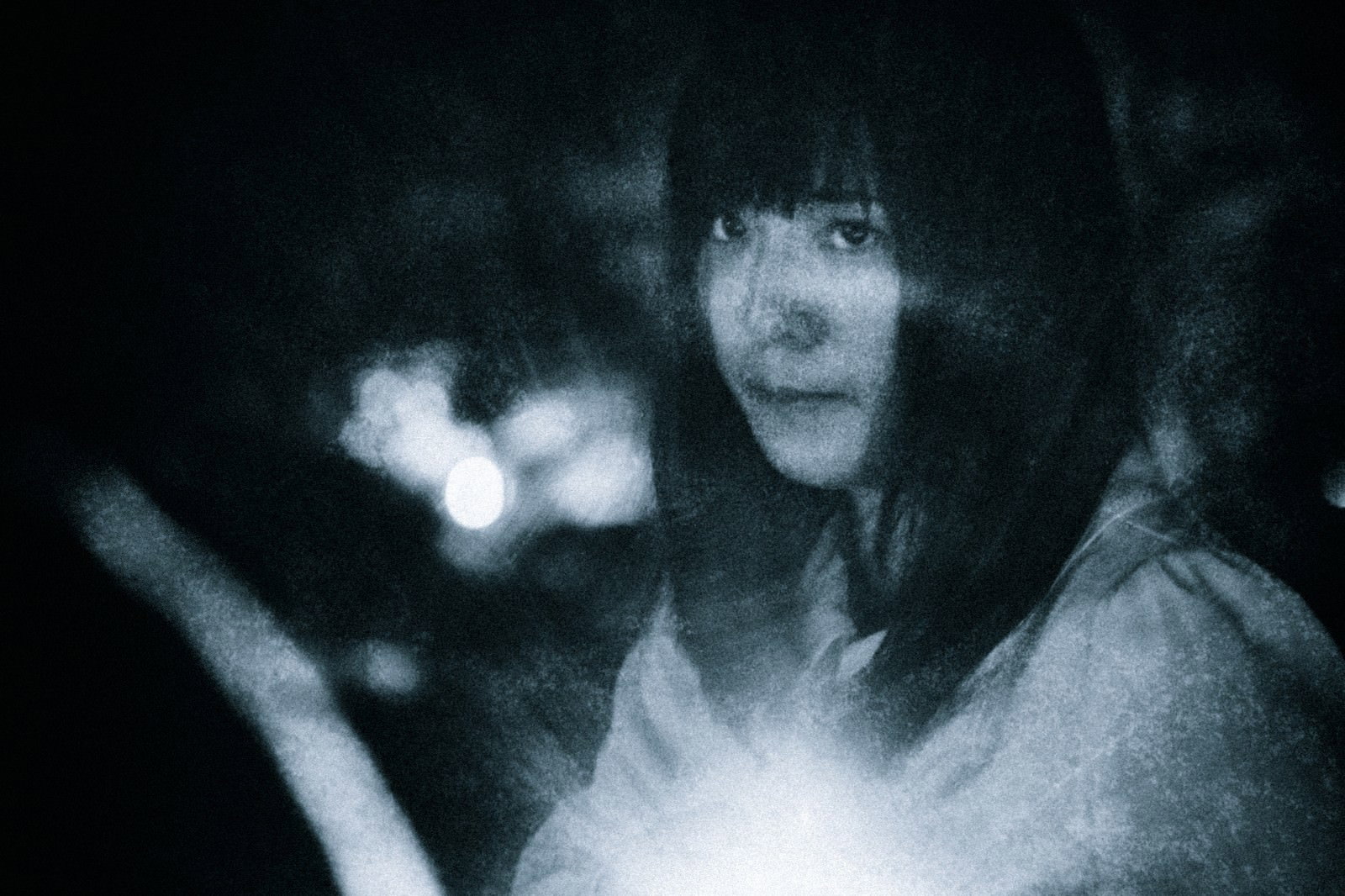 懐中電灯を持ち不安な表情で暗闇を進む女性［モデル：さとうゆい］