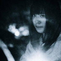 懐中電灯を持ち不安な面持ちで暗闇を進む女性の写真