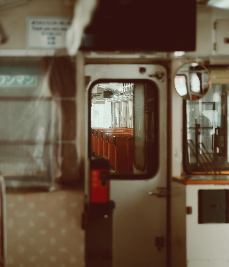 クリーム色と赤褐色の車体の古い電車の車内で、赤い手すりと窓枠が見える