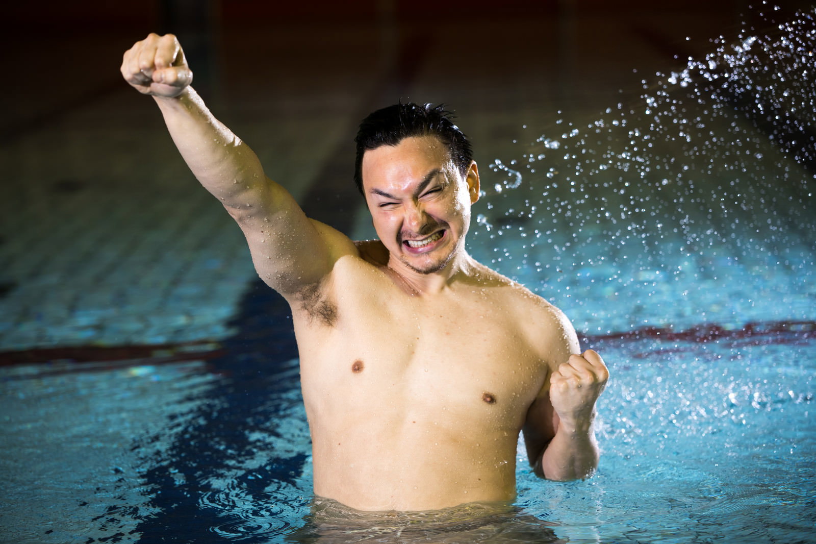プールで水しぶきを上げながらガッツポーズを決める男性［モデル：Max_Ezaki］