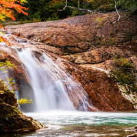秋の紅葉に包まれた赤滝と水飛沫が舞う清流の風景の写真