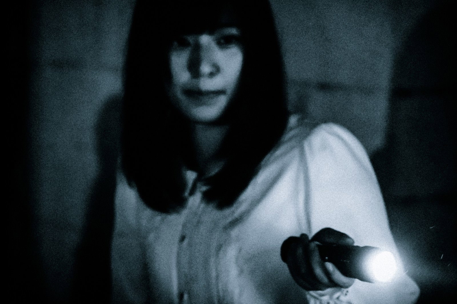 暗闇の中で懐中電灯の光に照らされる女性の写真［モデル：さとうゆい］