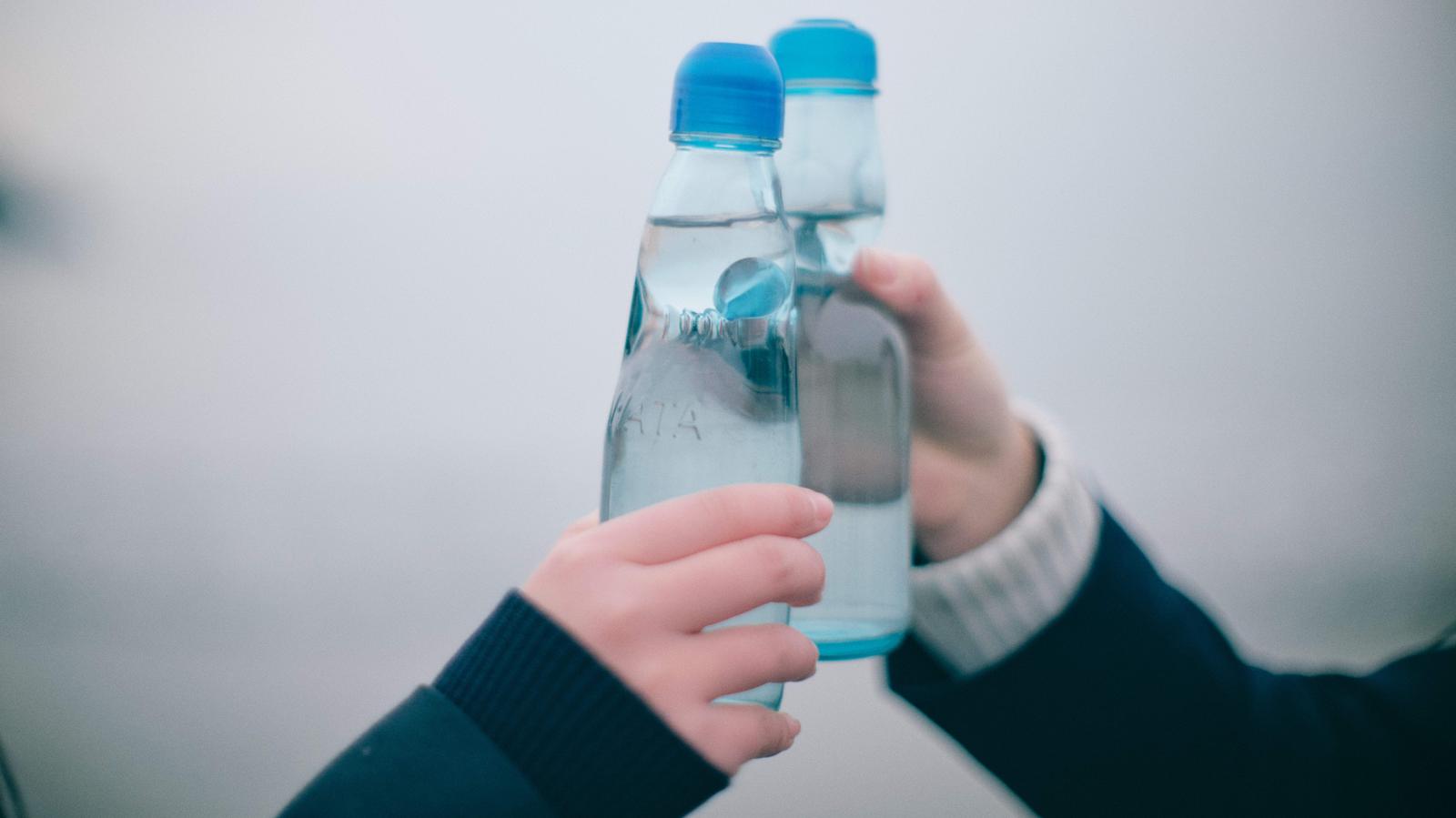 ラムネ瓶を重ね合わせて乾杯する女子高生の手元のクローズアップ