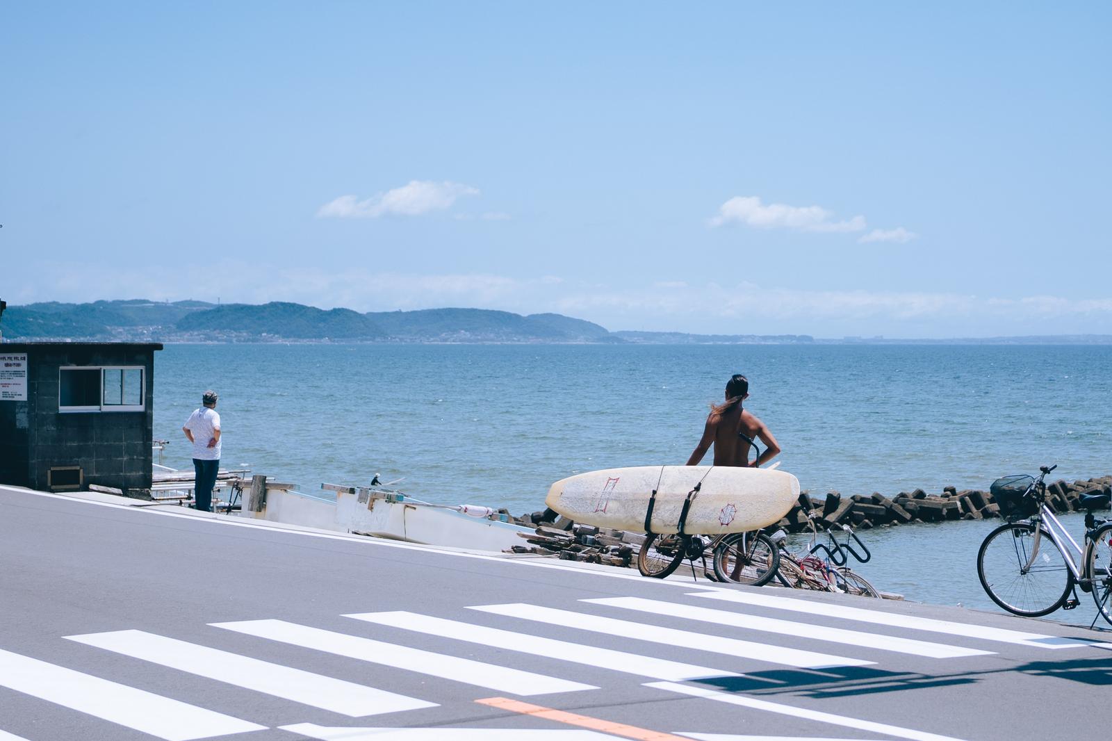 海沿いの堤防でサーフボードを持つサーファーと停められた自転車
