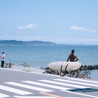 海沿いの横断歩道とサーファー、自転車とサーフボードの写真