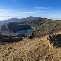 蔵王山の荒涼とした斜面に点在する噴石と御釜の火口湖の写真