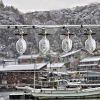 雪が降る港に一列に吊るされた照明ライトと船舶の写真