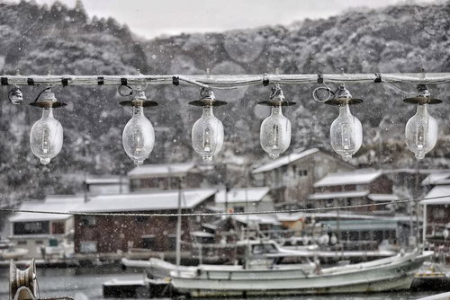 雪が降る港に一列に吊るされた照明ライトと船舶