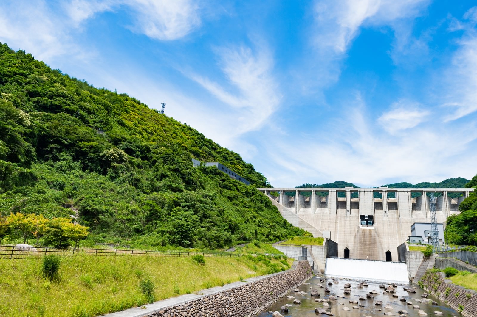 青空の下、緑の山々に囲まれた苫田ダムと奥津湖の風景