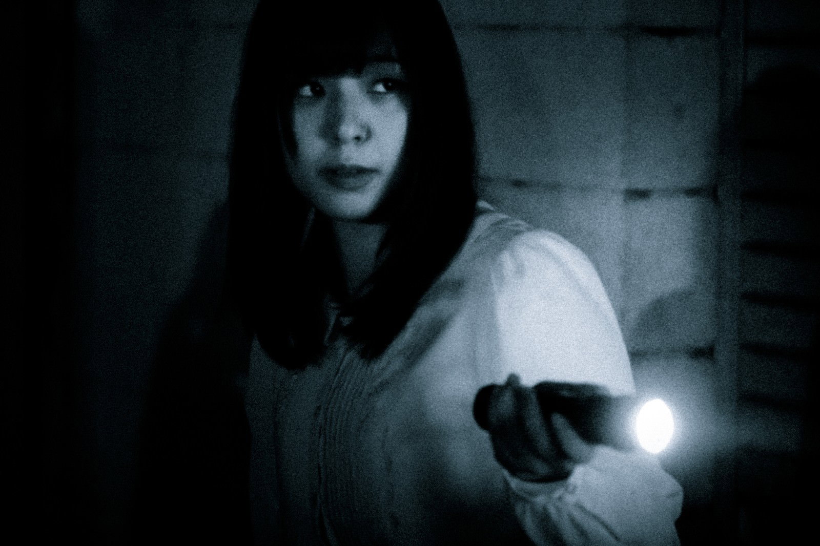 暗闇の中で懐中電灯を持ち前方を照らす長髪の女性［モデル：さとうゆい］