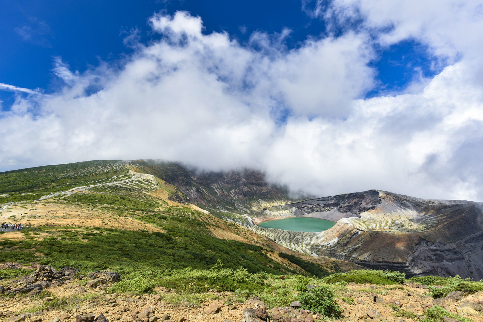 青空と雲の下に広がる蔵王山の火口湖御釜とその周辺の山々
