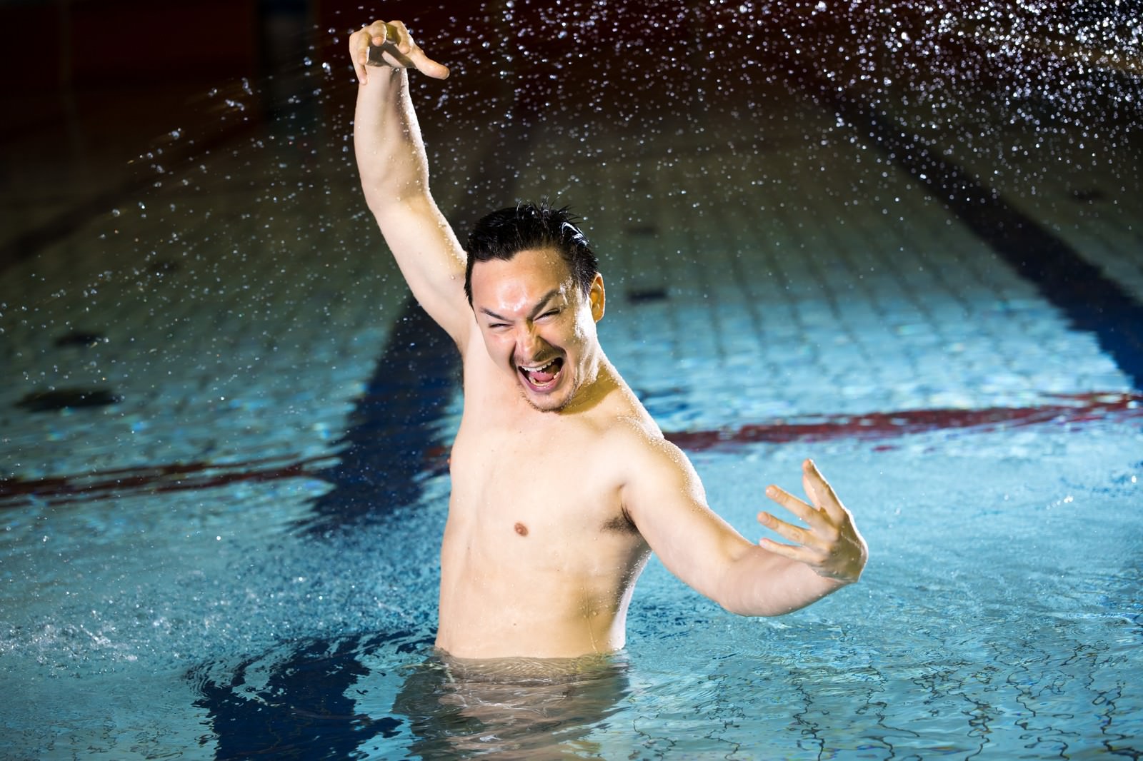 屋内プールの水中で両腕を上げ、口を大きく開けて叫んでいる男性［モデル：Max_Ezaki］