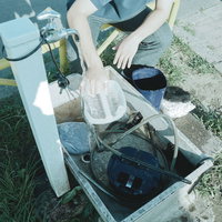公園の水道で外部濾過装置を洗う男子高校生の写真
