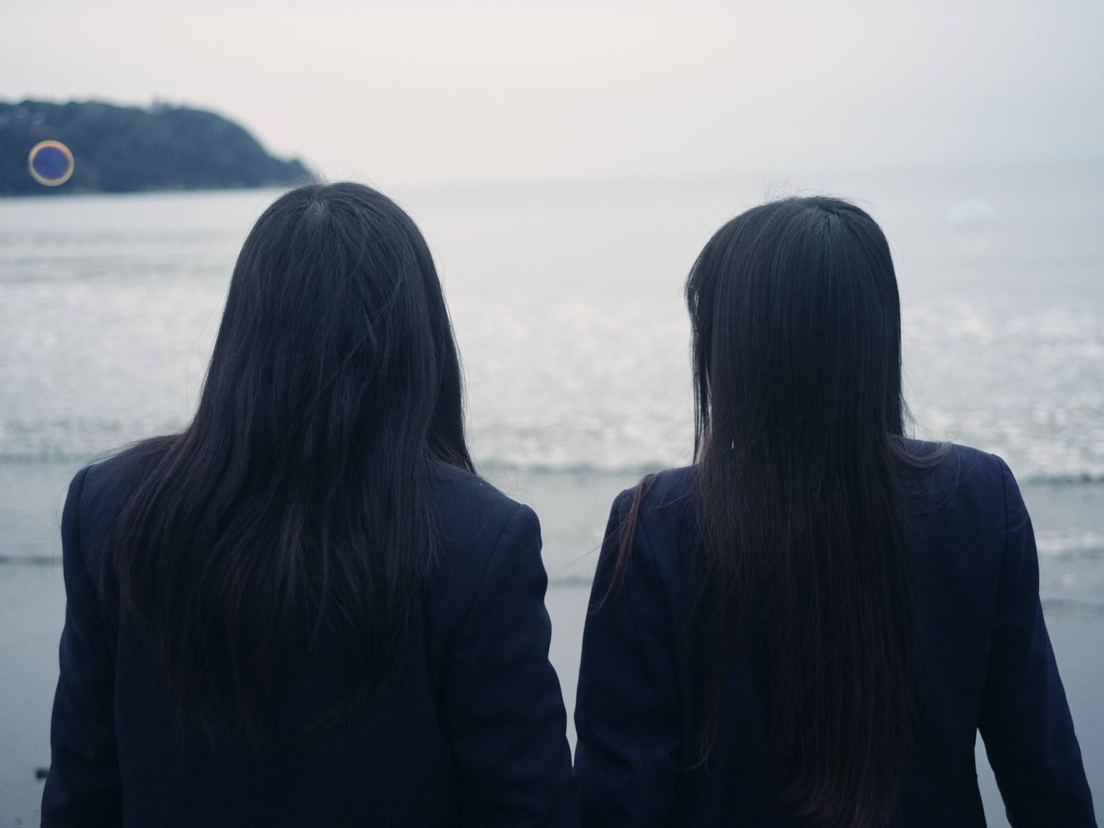海岸で海を眺める制服姿の女子高生ふたり