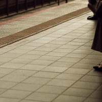 通勤時間帯の駅ホームの点字ブロックと乗客の足元の写真