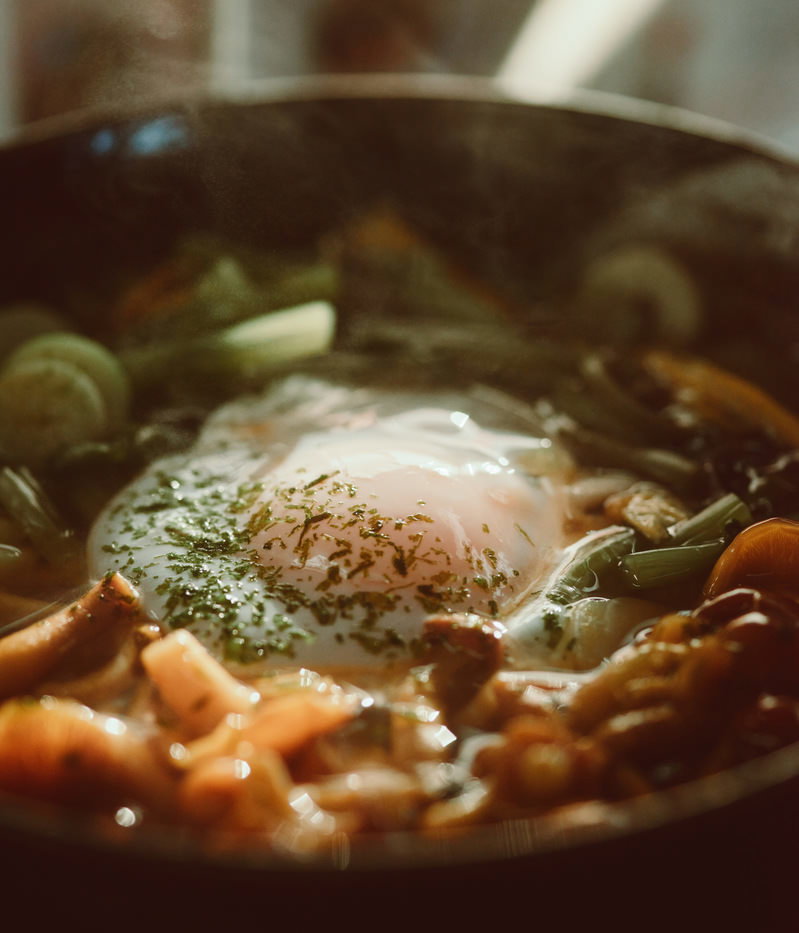 温泉卵がのった熱い卵うどん、青ねぎと薬味がトッピングされた丼
