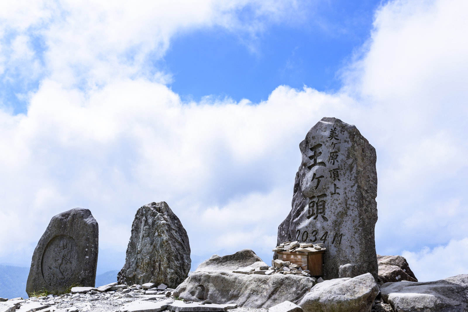 青空と雲を背景に陽光を浴びる美ヶ原王ヶ頭の山頂石碑