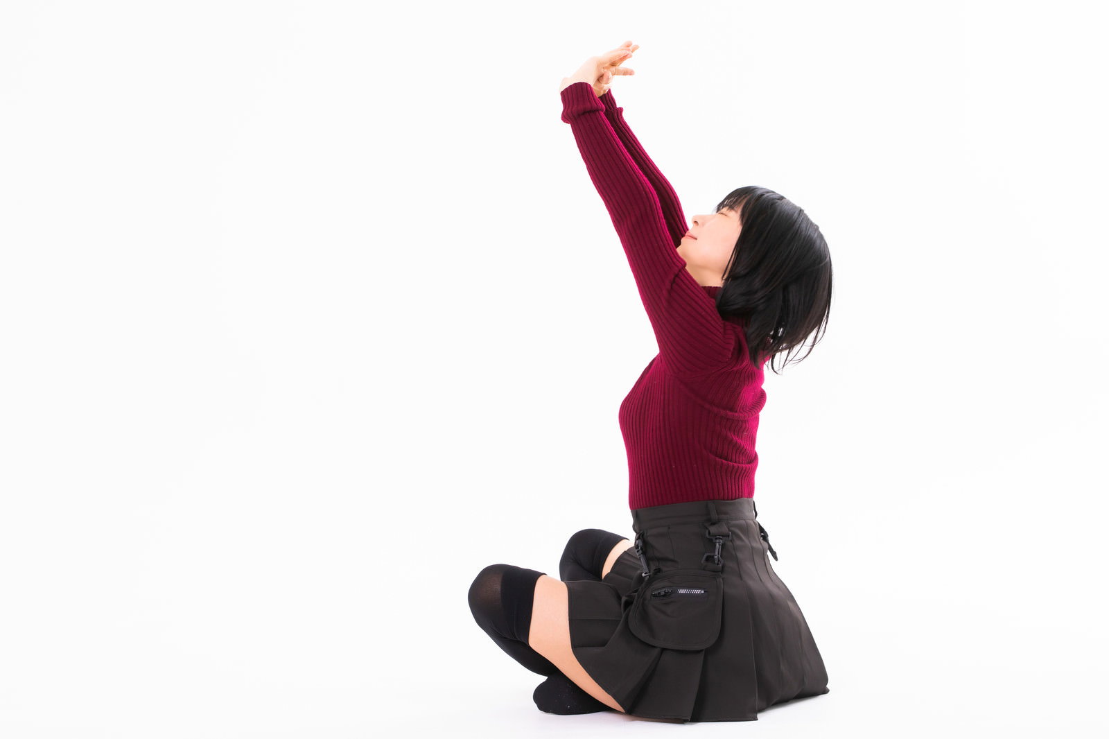 胡坐をかいて両手を上に伸ばしてストレッチする赤いトップスの女性［モデル：にゃるる］