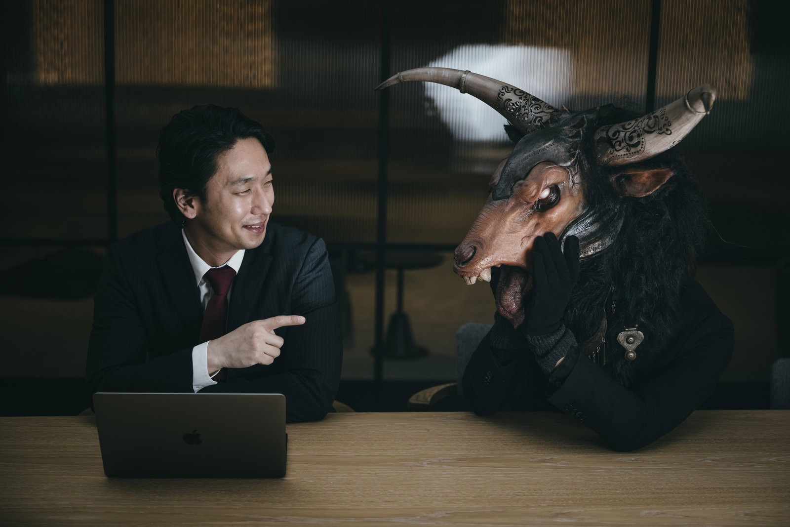 暗い室内で魔神と向き合い談笑する会社員