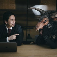暗い室内で魔神と談笑する会社員の写真