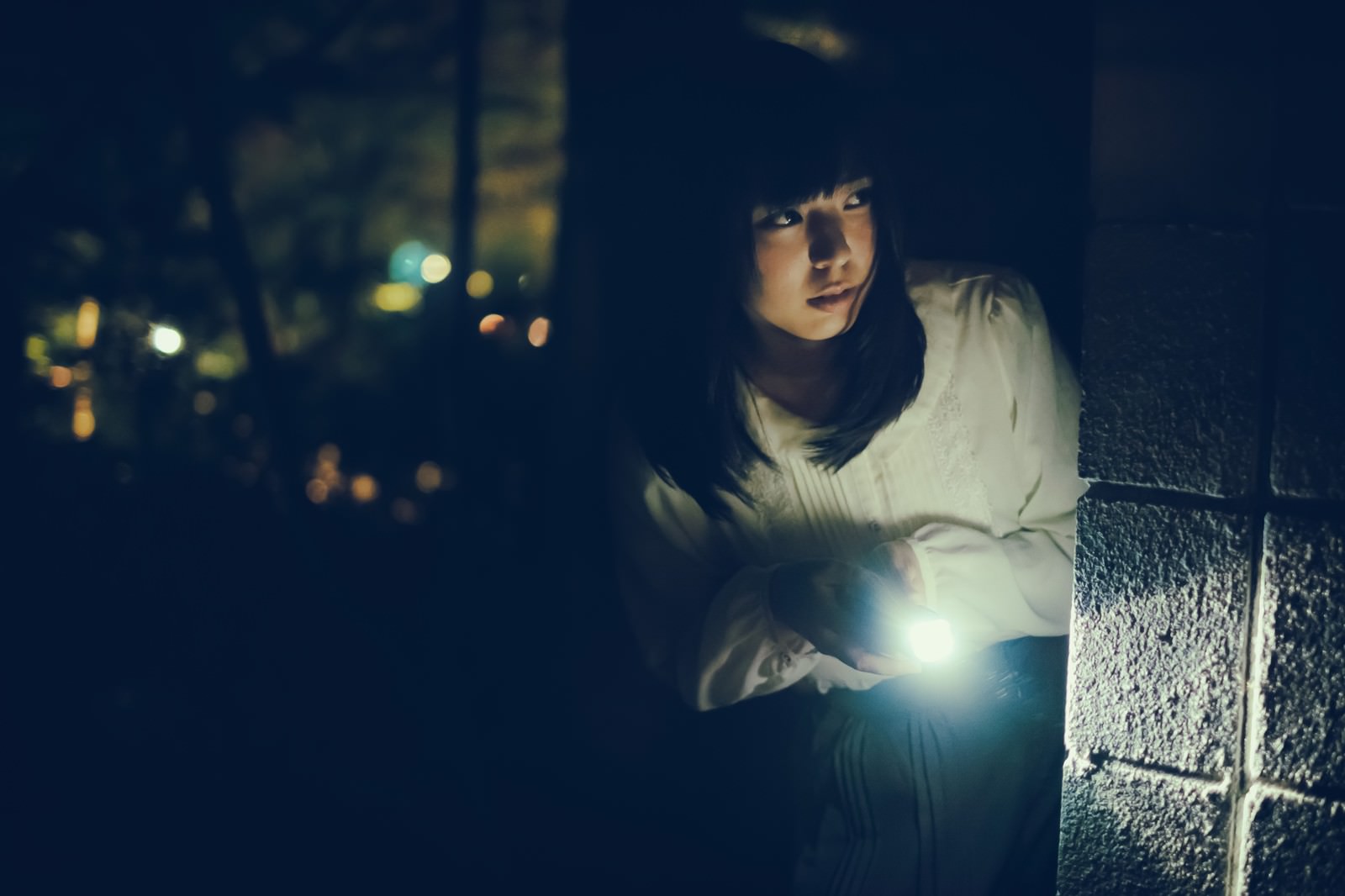 暗闇の中で懐中電灯を手に持つ女性の姿［モデル：さとうゆい］