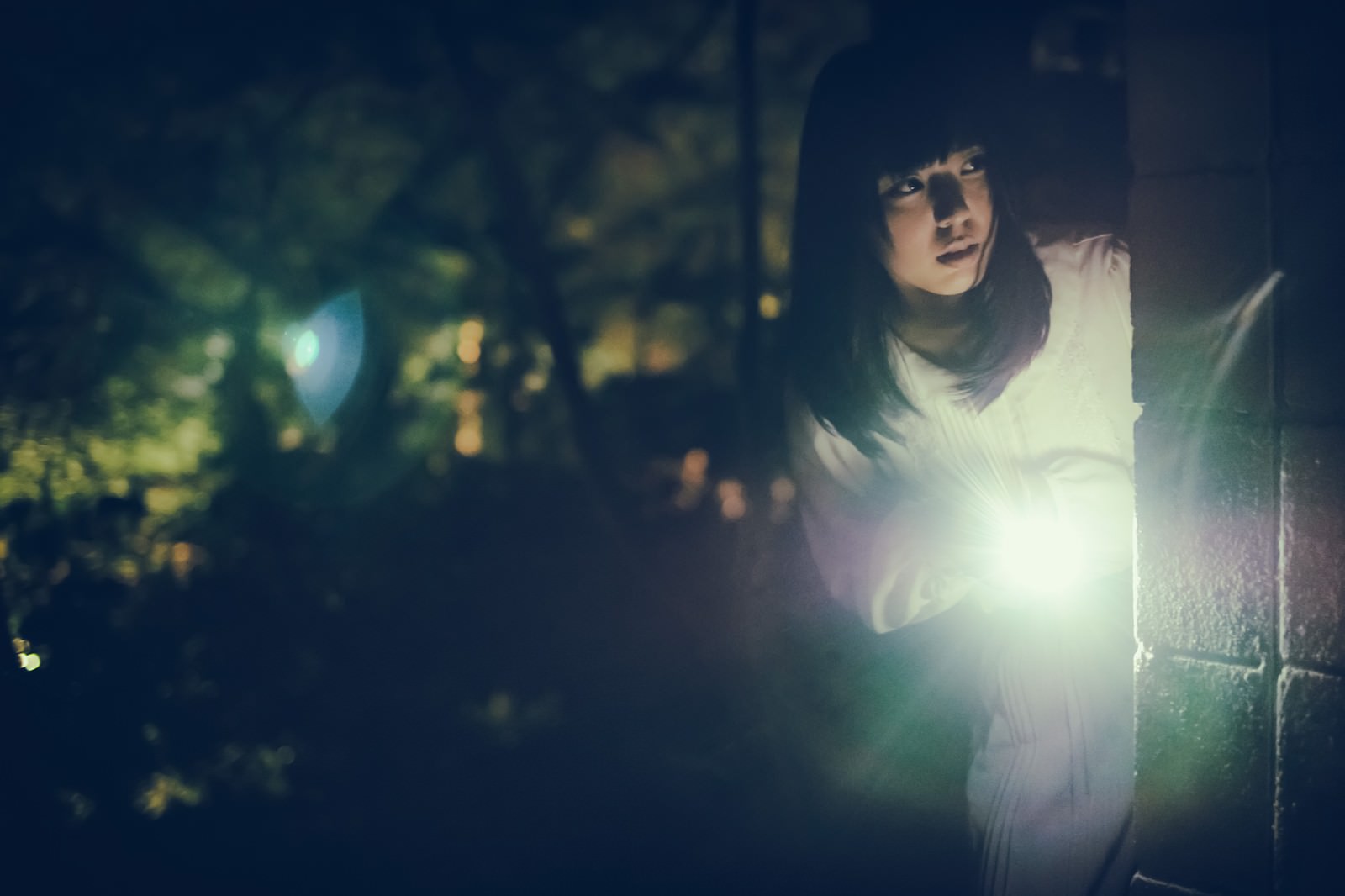 暗闇の中で懐中電灯を持ちながら周囲を警戒している女性［モデル：さとうゆい］