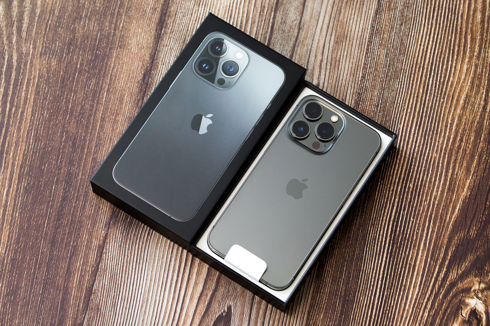 木目のテーブルの上でiPhone 13の黒い箱を開封している様子