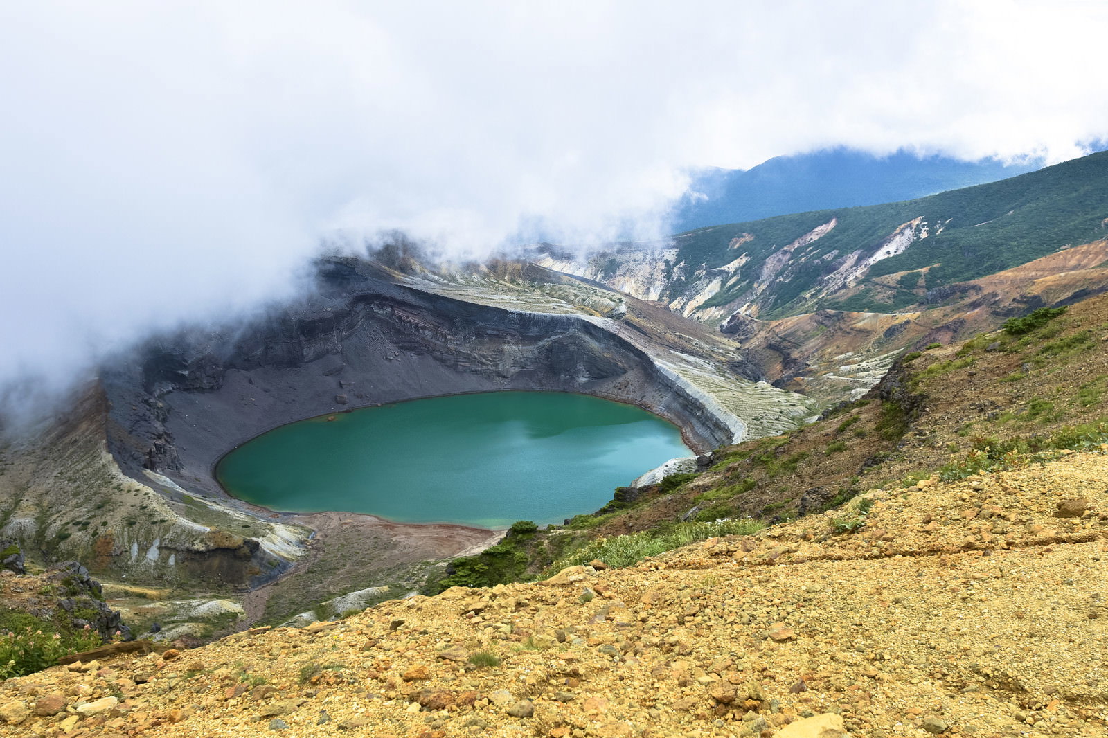 雲に包まれた蔵王山の御釜、エメラルドグリーンの火口湖が雲の合間から見える