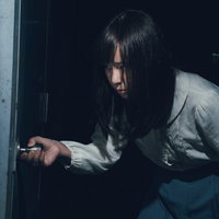 薄暗い空間で恐る恐る扉をあける女性の緊張した表情の写真