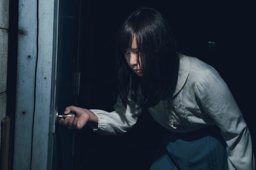 薄暗い空間で恐る恐る扉をあける女性の緊張した表情