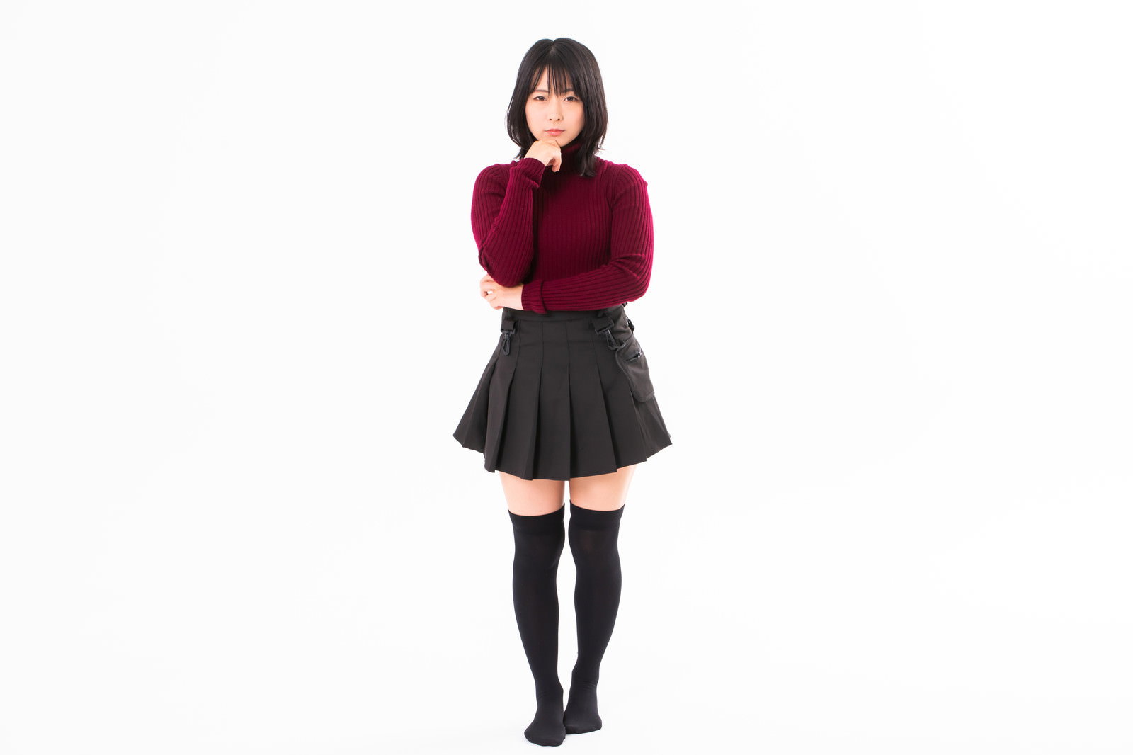 顎に手を当てて考えるポーズの女性、赤いニットと黒いスカート着用［モデル：にゃるる］