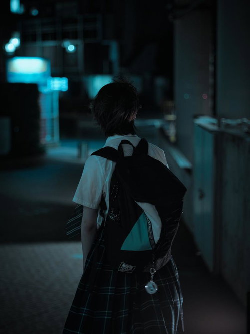 夜の街並みを歩く制服姿の女子高生の後ろ姿