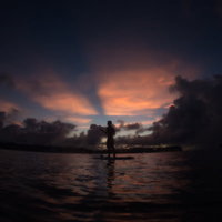 夕暮れの海でパドルボートを漕ぐ男性のシルエットの写真