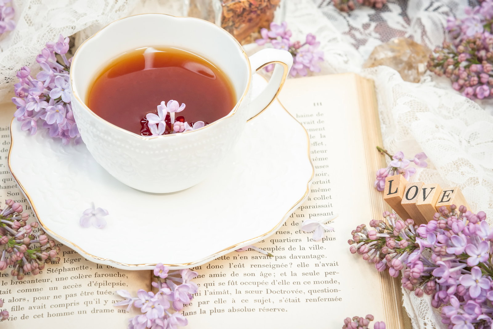 白いティーカップに紅茶が注がれ、薄紫色のライラックの花と洋書が周りに配置されている