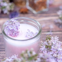 白いキャンドルに飾られたライラックの花のアレンジメントの写真