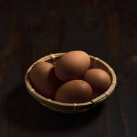卓上の竹かごに入った生卵と新鮮な食材の写真