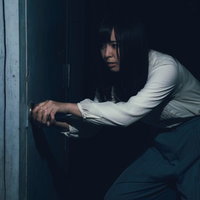 古びたドアを恐る恐る開ける白い服の女性の不安な表情の写真