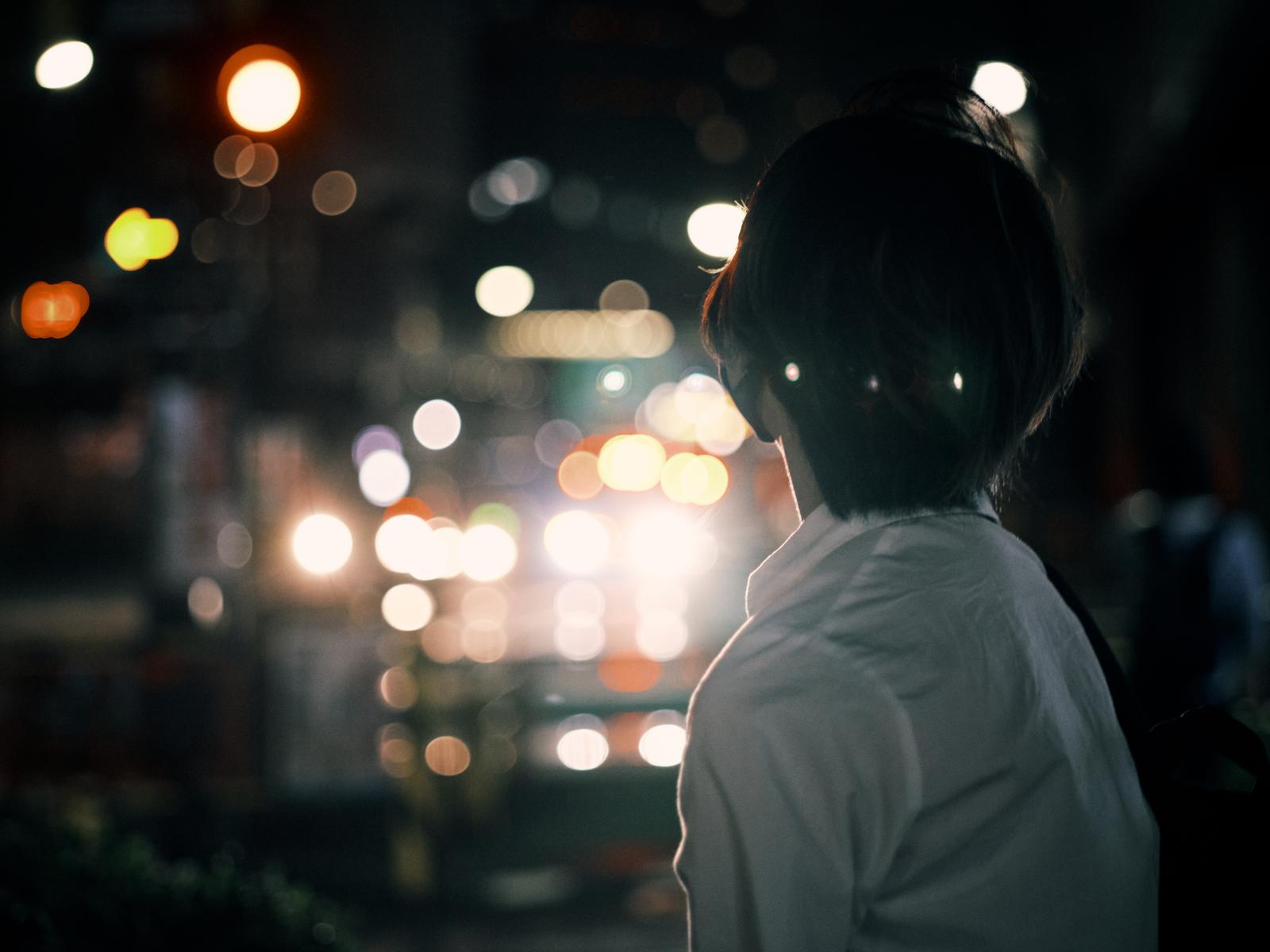 ネオン街の夜景を背景に立つ高校生の後ろ姿
