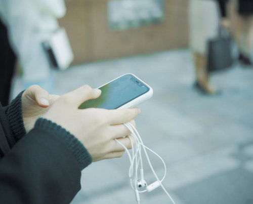 有線イヤホンを持ちながらスマホを操作する女子高生の手元