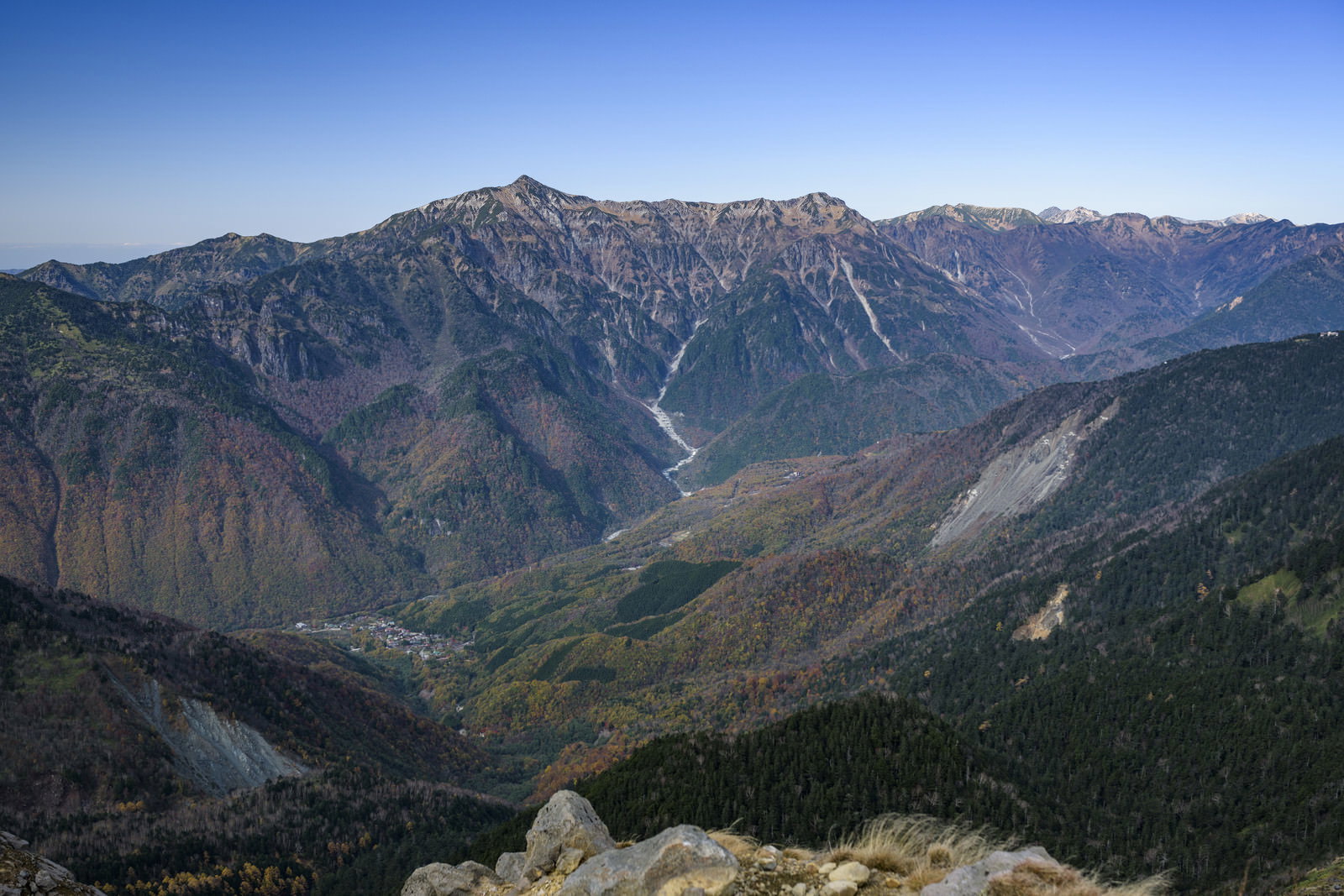 青空の下、中腹が紅葉で色づいた笠ヶ岳と連なる山々の稜線
