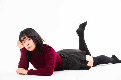 赤い長袖で頬杖をついて横たわるポージング中の女性