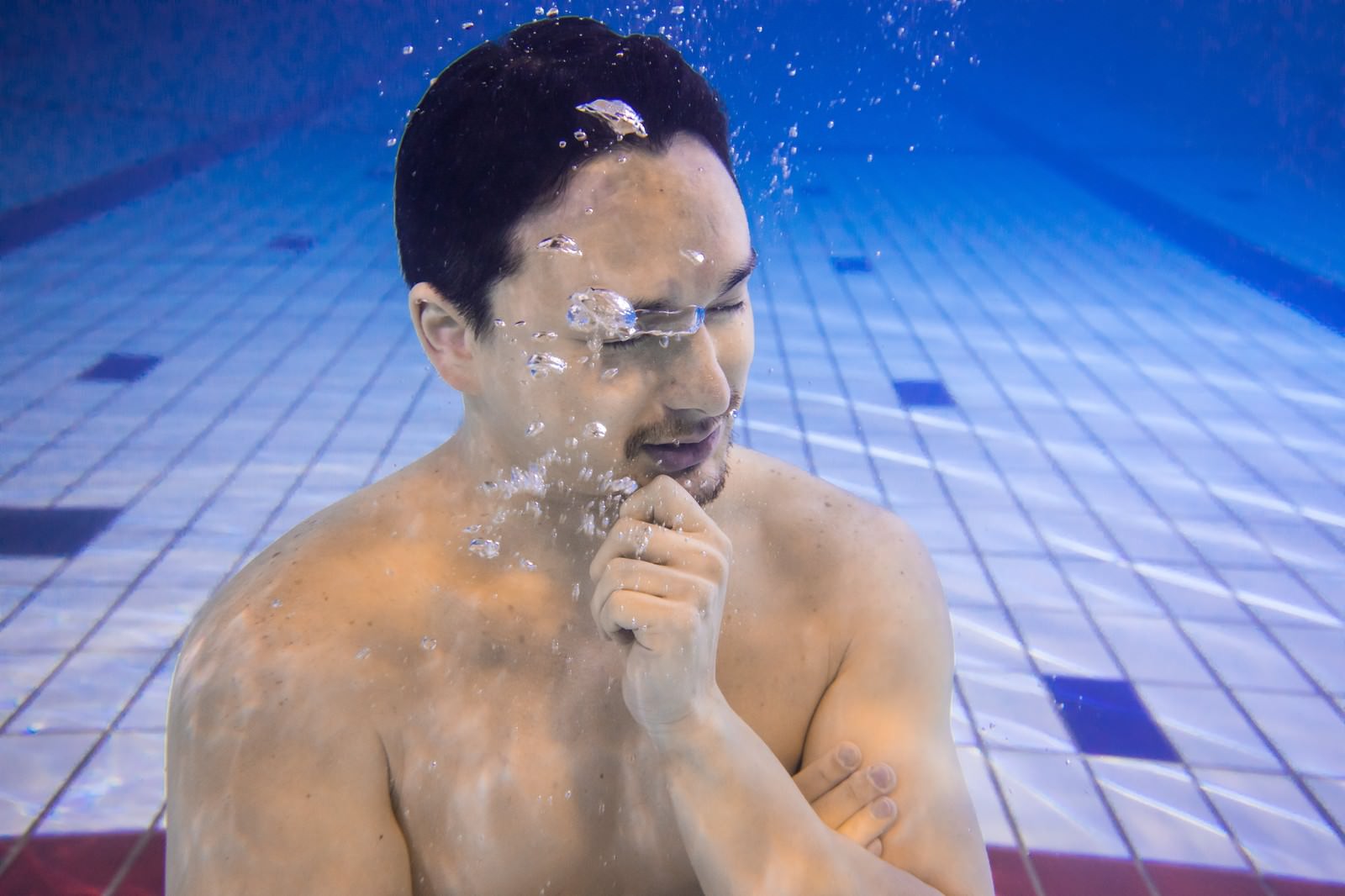 プールの水中で目を閉じて考え込んでいる男性［モデル：Max_Ezaki］
