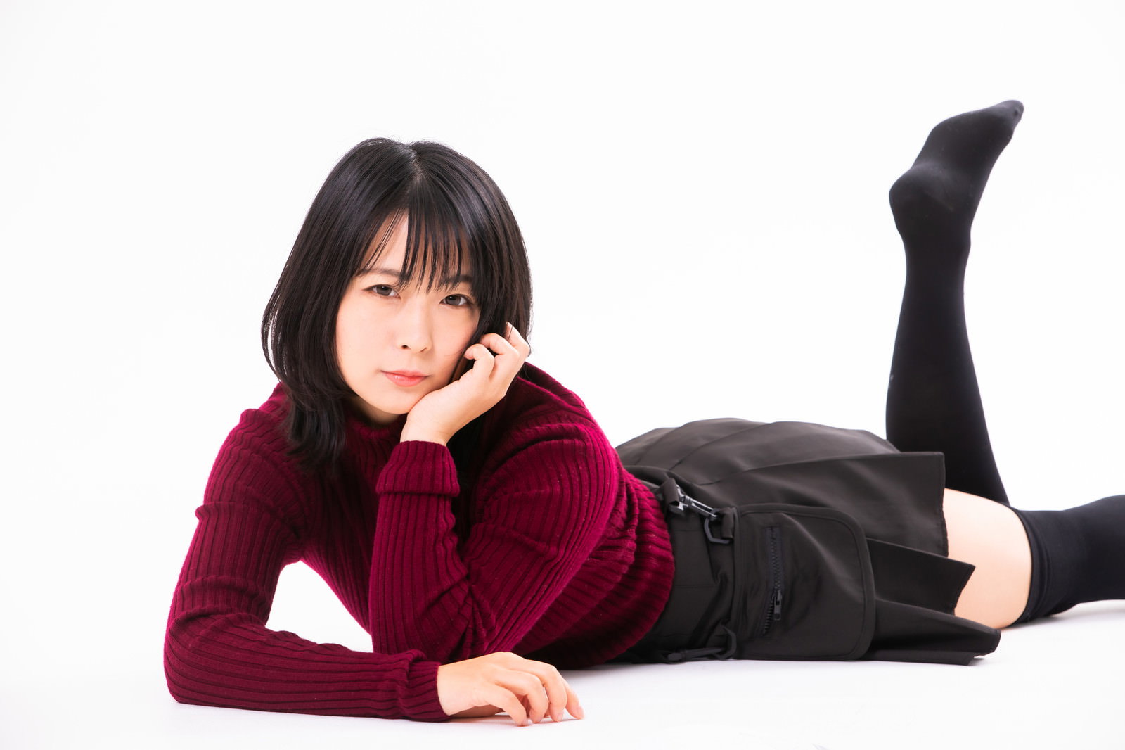 ワインレッドのニットを着た女性が床で頬杖をついている［モデル：にゃるる］