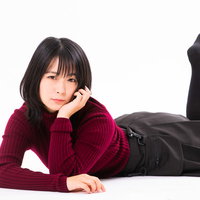 ワインレッドのニットを着て頬杖を突いて横たわる女性の写真