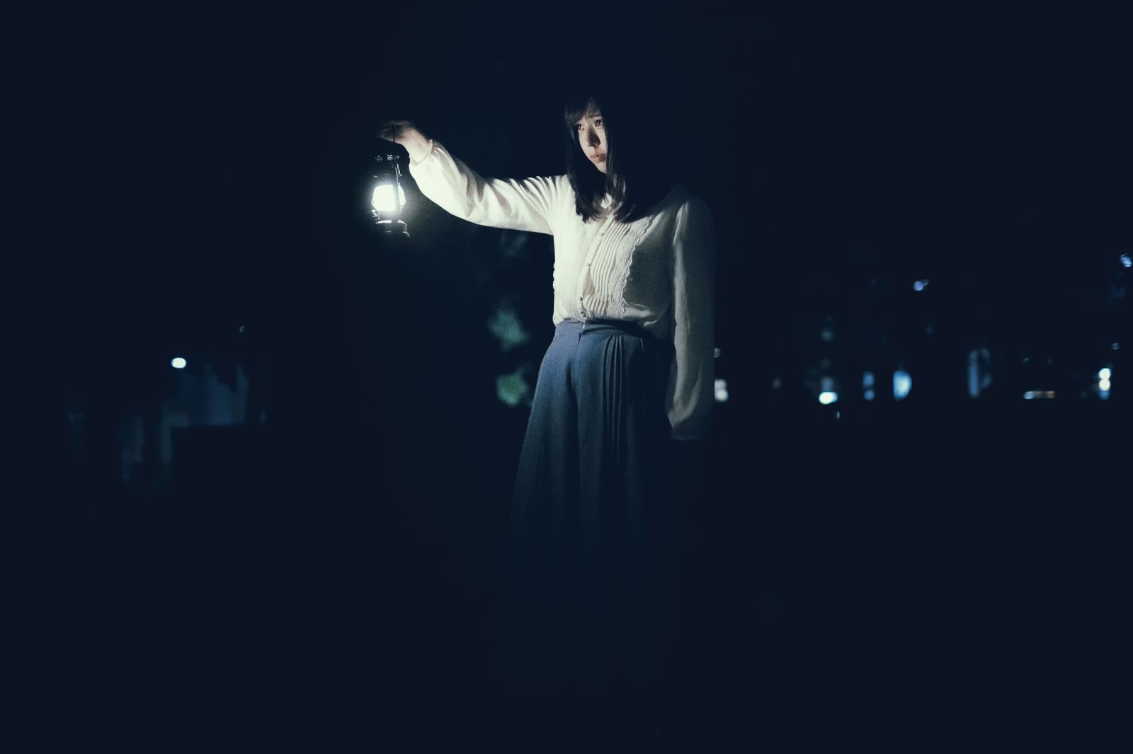 暗い夜道でランタンを手に持ち立っている女性［モデル：さとうゆい］