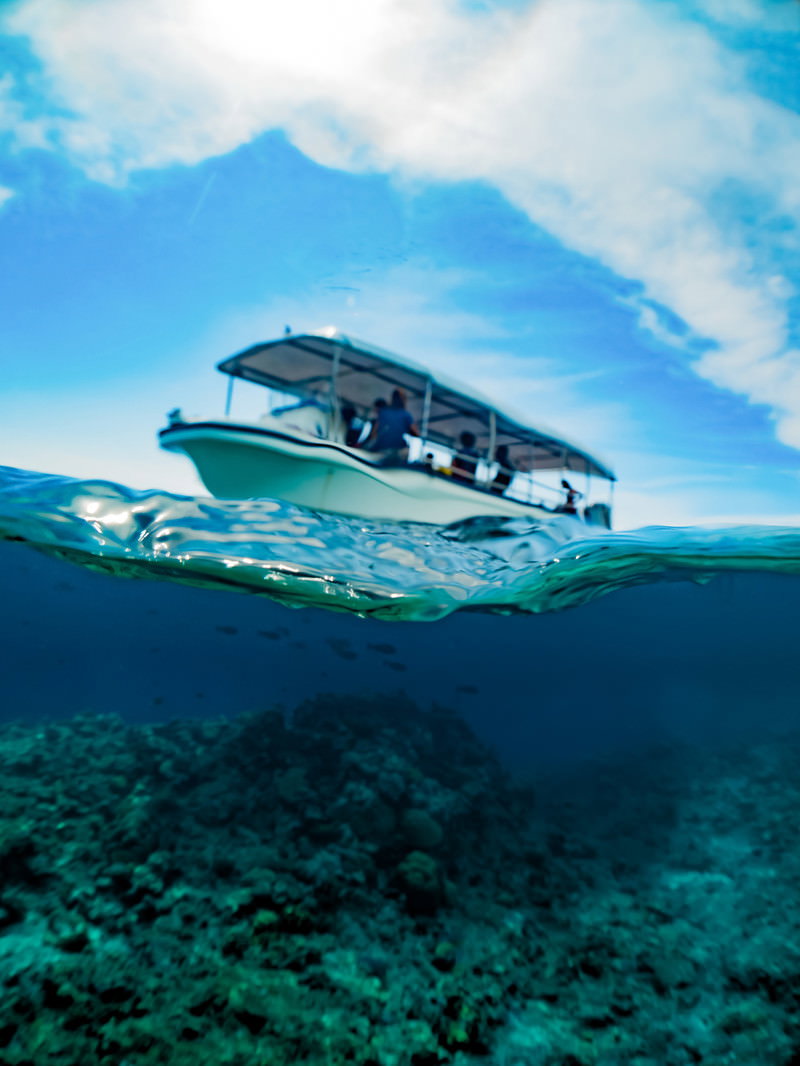 青い海の水面に浮かぶ観光ボートを水中から撮影した写真